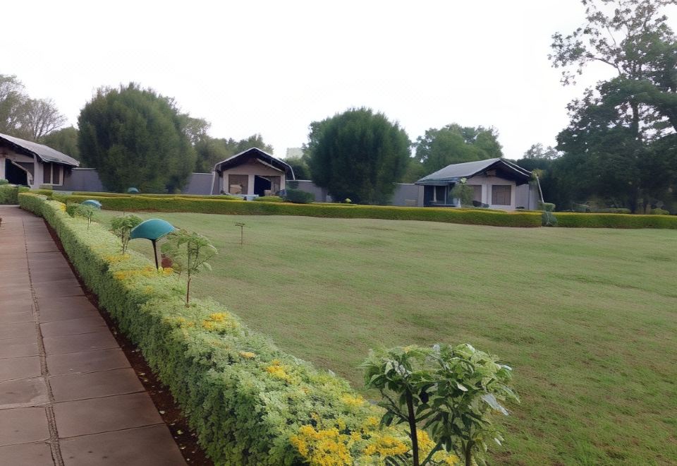 a grassy field with two small houses in the background , surrounded by trees and bushes at Spice Garden
