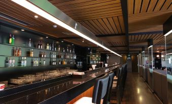 a well - lit bar with a long wooden bar , several chairs , and a variety of bottles and glasses on display at Forbis Hotel