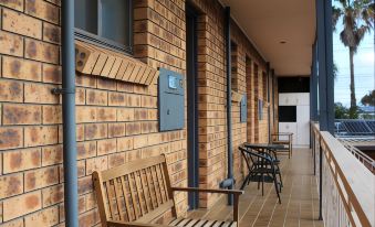 a wooden bench and two chairs are placed on a porch next to a brick wall at Bridge View Motel