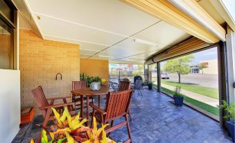 a patio with a wooden dining table and chairs , surrounded by potted plants and a brick wall at Raintree Motel