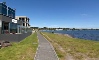 a paved walkway next to a body of water , with a man riding a bike on the path at The Cove