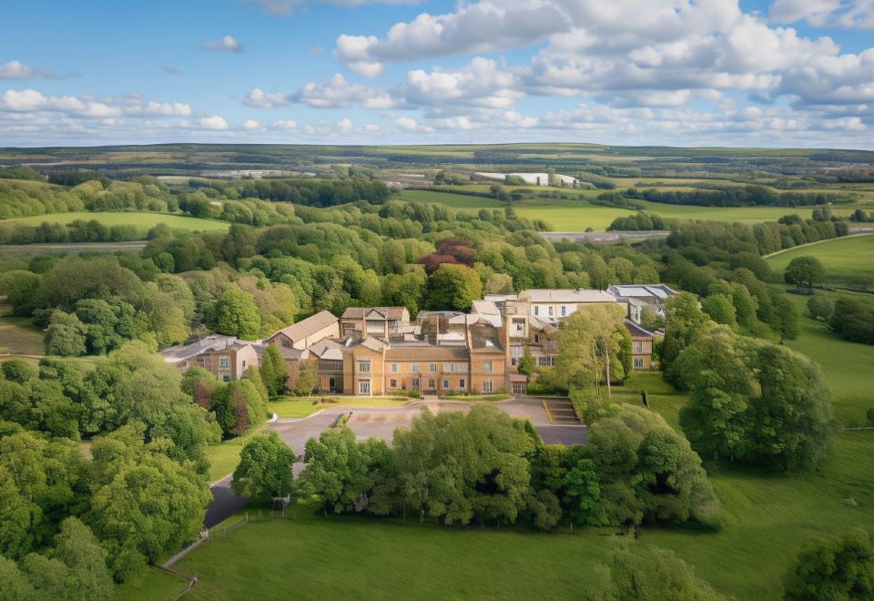 aerial view of a large building surrounded by lush green grass and trees , with a body of water in the background at Mercure Blackburn Dunkenhalgh Hotel & Spa