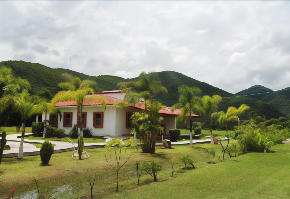 a house with a red roof is surrounded by green grass and palm trees , with mountains in the background at Las Jaras Aguas Termales
