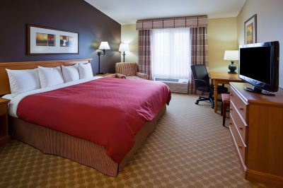 a hotel room with a large bed , desk , and window , decorated in warm colors and style at Country Inn & Suites by Radisson, Watertown, SD