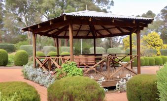 a wooden gazebo surrounded by a lush garden , with various plants and trees in the background at Travellers Rest Motel
