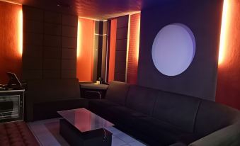 a modern living room with a black couch , glass coffee table , and circular window in the background at Hotel Sri Bernam