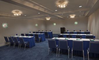 a conference room with blue chairs and tables , chandeliers , and a stage at the end at Delray Sands Resort