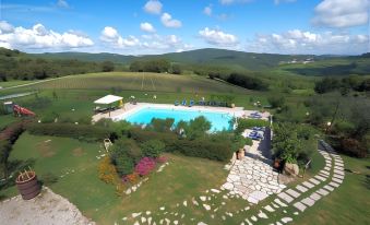 a large outdoor pool surrounded by green grass and trees , with a view of the countryside at Antico Borgo Il Cardino