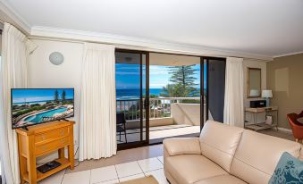 a living room with a couch , television , and sliding glass doors leading to an ocean view balcony at Coolum Caprice