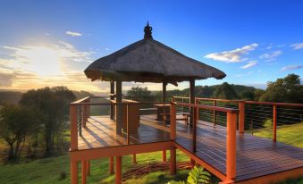 a wooden deck with a thatched roof , surrounded by lush greenery and the setting sun at Maleny Tropical Retreat