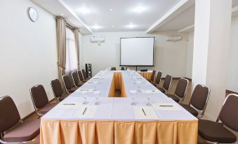 a large conference room with multiple tables and chairs , a projector screen , and water bottles at Sevilla Resort Magelang