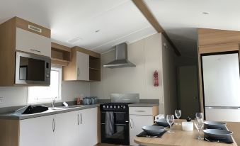 a modern kitchen with white cabinets , a black stove and oven , a dining table with wine glasses , and a window at Premier Inn Newquay (Quintrell Downs)