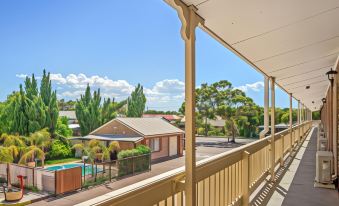 a balcony overlooking a pool and a hot tub , surrounded by trees and a blue sky at Motel Goolwa