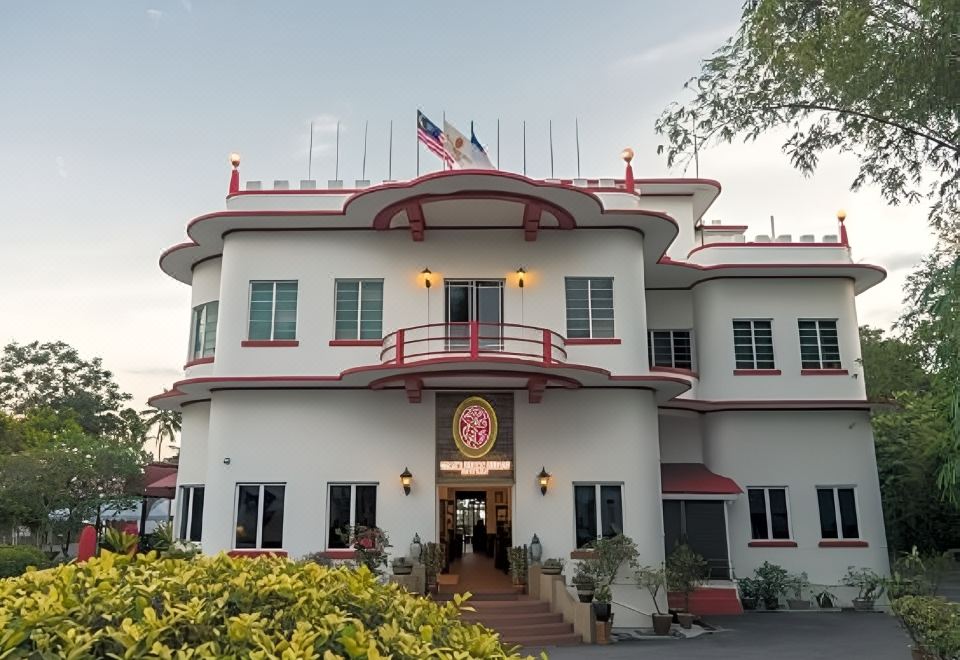 a large white building with red trim , situated in a park - like setting , surrounded by trees at Shah's Beach Resort Malacca