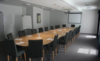 a conference room with a long wooden table , chairs , and a projector screen , set up for a meeting or presentation at Days Inn by Wyndham London Stansted Airport
