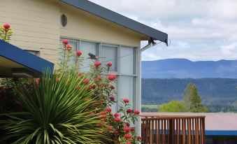 a house with a view of mountains , surrounded by greenery and a fence , including a bush with red flowers at Mountain View Country Inn