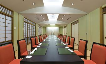 a long conference table with red chairs , green placemats , and a menu board , set in a dimly lit room with windows at Hotel Verde