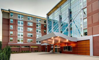 a modern hotel building with multiple floors , large windows , and a red brick facade , situated on a sunny day at Aloft Chapel Hill