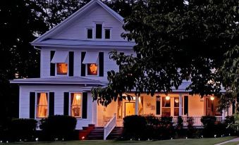 a large white house with black shutters and a red porch is lit up at night at Whole Hearts Bed and Breakfast