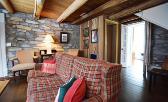 a cozy living room with a plaid couch , wooden walls , and a stone fireplace , decorated with pictures on the walls at Graves Mountain Farm & Lodges