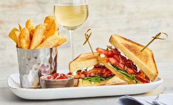 a plate of food with a sandwich , fries , and a glass of white wine on a table at Courtyard Birmingham Homewood