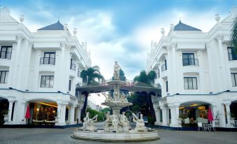 a large white fountain in the middle of a plaza , surrounded by buildings and palm trees at Ramada Suites by Wyndham Solo