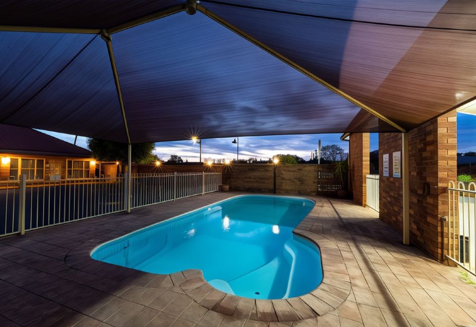 a large swimming pool is surrounded by a patio with a roof , and the surrounding area is lit up at night at Parkes International
