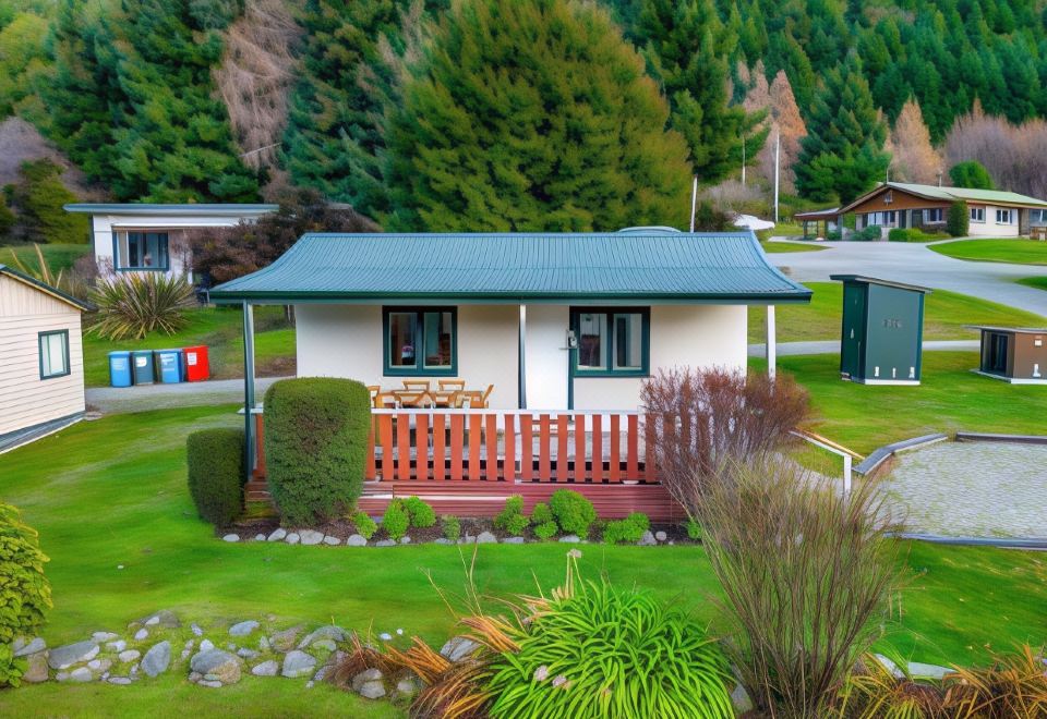 a small white house with a green roof and a picket fence in front of it at The Camp - Lake Hawea