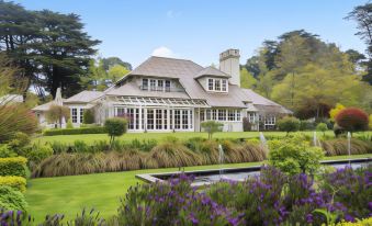 a large house surrounded by a lush green lawn , with a fountain in the foreground at Parklands Country Gardens & Lodges Blue Mountains