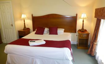 a well - lit hotel room with a wooden bed , white sheets , and a red blanket , along with two lamps on either side of the at The Atherstone Red Lion Hotel