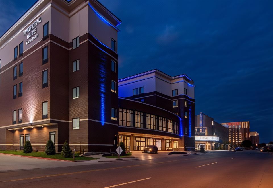 a large , modern building with multiple floors and blue lights is situated on a street at night at SpringHill Suites Oklahoma City Downtown/Bricktown