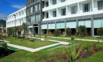 a modern building with white and gray balconies is surrounded by a green lawn and trees at Hotel Vale Do Navio