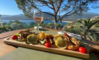 a wooden tray filled with various food items , including seafood and fruits , placed on a dining table near a window at A’mare Corsica Seaside Small Resort