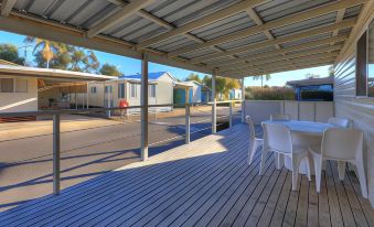 a wooden deck with white chairs and a table is surrounded by blue and white tents at Nambucca River Village by Lincoln Place