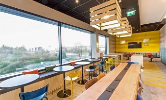 a modern , well - lit dining room with large windows offering views of the city , wooden tables and chairs , and a central counter at Ibis Styles Geneve Palexpo Aeroport