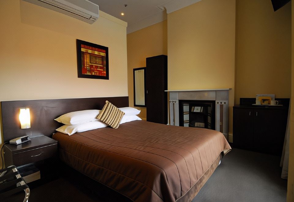 a well - lit hotel room with a large bed , brown bedding , and a painting on the wall at Captain Cook Hotel