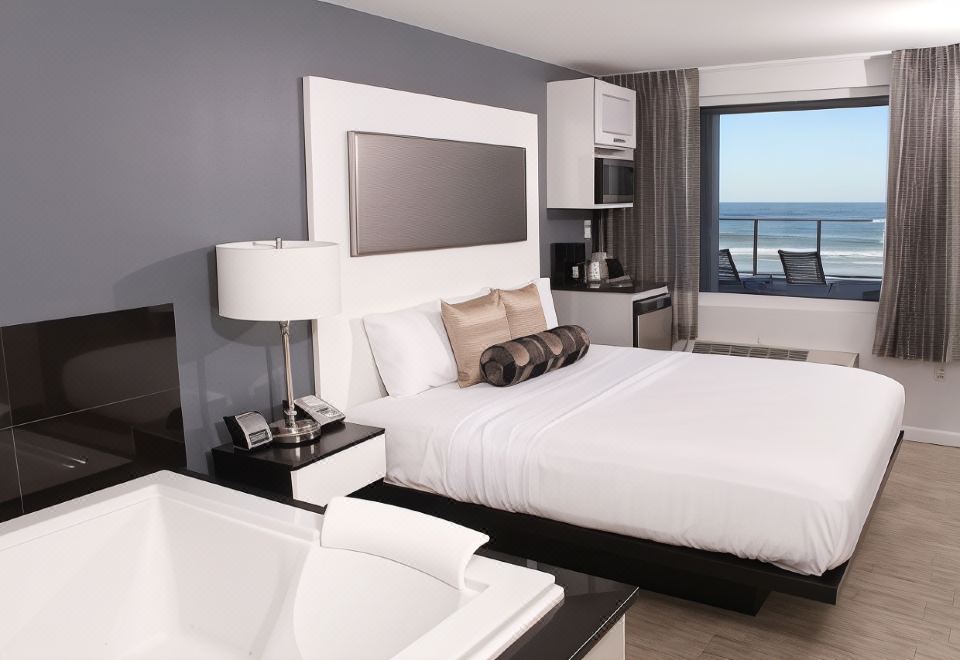 a modern bedroom with a white bed , black headboard , and large windows overlooking the ocean at Lotus Boutique Inn and Suites