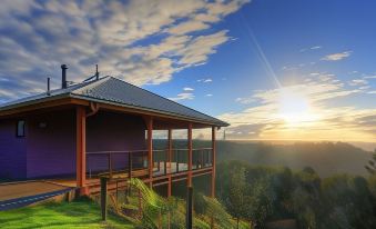 a wooden house with a purple roof sits on a hillside , overlooking a beautiful sunrise at Maleny Tropical Retreat