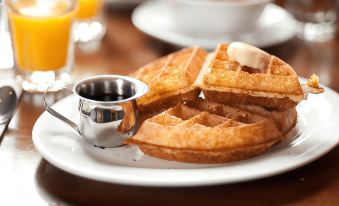 a plate of waffles with syrup and butter is placed on a table next to other breakfast items at The Upper House Hotel