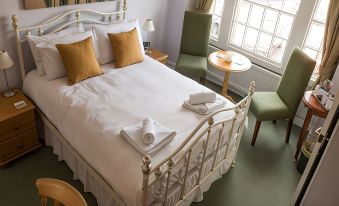 a large bed with white linens and gold throw pillows is in a room with green carpet , chairs , and a window at Phelips Arms
