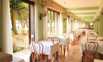 an empty restaurant with tables and chairs , white tablecloths , and large windows overlooking a lush green garden at Hotel Stella d'Italia