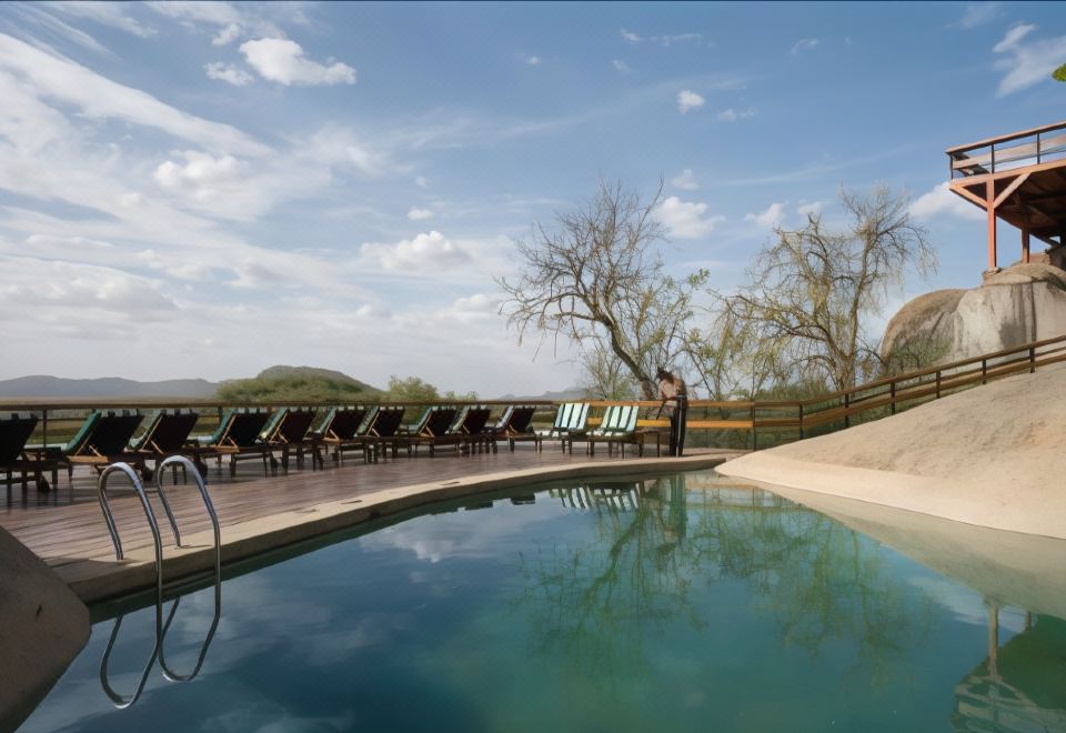 a man standing near a pool with lounge chairs and trees in the background at Seronera Wildlife Lodge