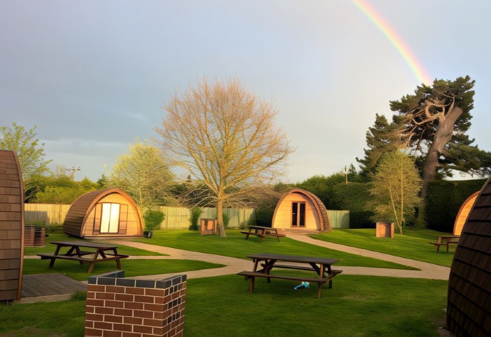 a group of two small wooden cabins situated in a grassy field , with a rainbow arching over them at King's Lynn Caravan & Camping Park