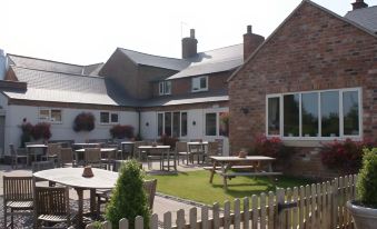 a brick building with a large open area in front of it , where several tables and chairs are set up for outdoor dining at The Sun Inn