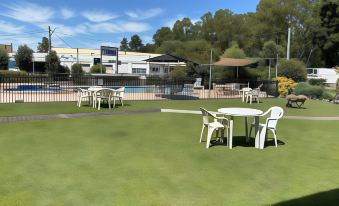 a green lawn with several white plastic chairs and tables , surrounded by trees and buildings at Bucketts Way Motel