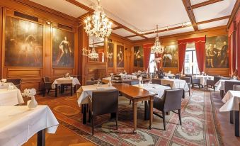 a large dining room with wooden tables , chairs , and a chandelier hanging from the ceiling at Fletcher Hotel Paleis Stadhouderlijk Hof