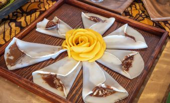 a wooden tray with a yellow rose - shaped flower arrangement on it , surrounded by several plates of food at Siargao Island Villas