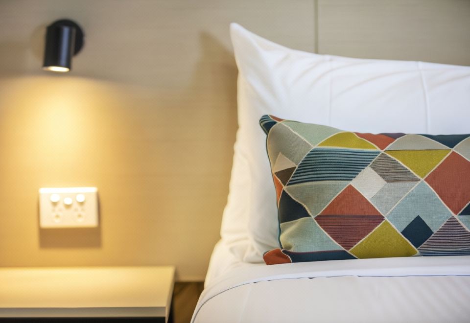 a bed with a colorful pillow and white sheets , situated next to a nightstand with a lamp at Nightcap at Sylvania Hotel