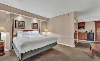 a hotel room with a king - sized bed , a flat - screen tv , and a kitchenette in the background at Buffalo Airport Hotel