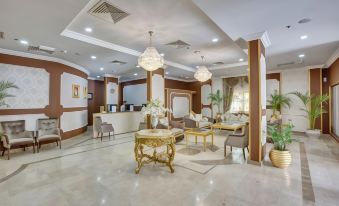 a luxurious lobby with a marble floor , chandeliers , and potted plants , as well as several chairs and tables at Royal Hotel